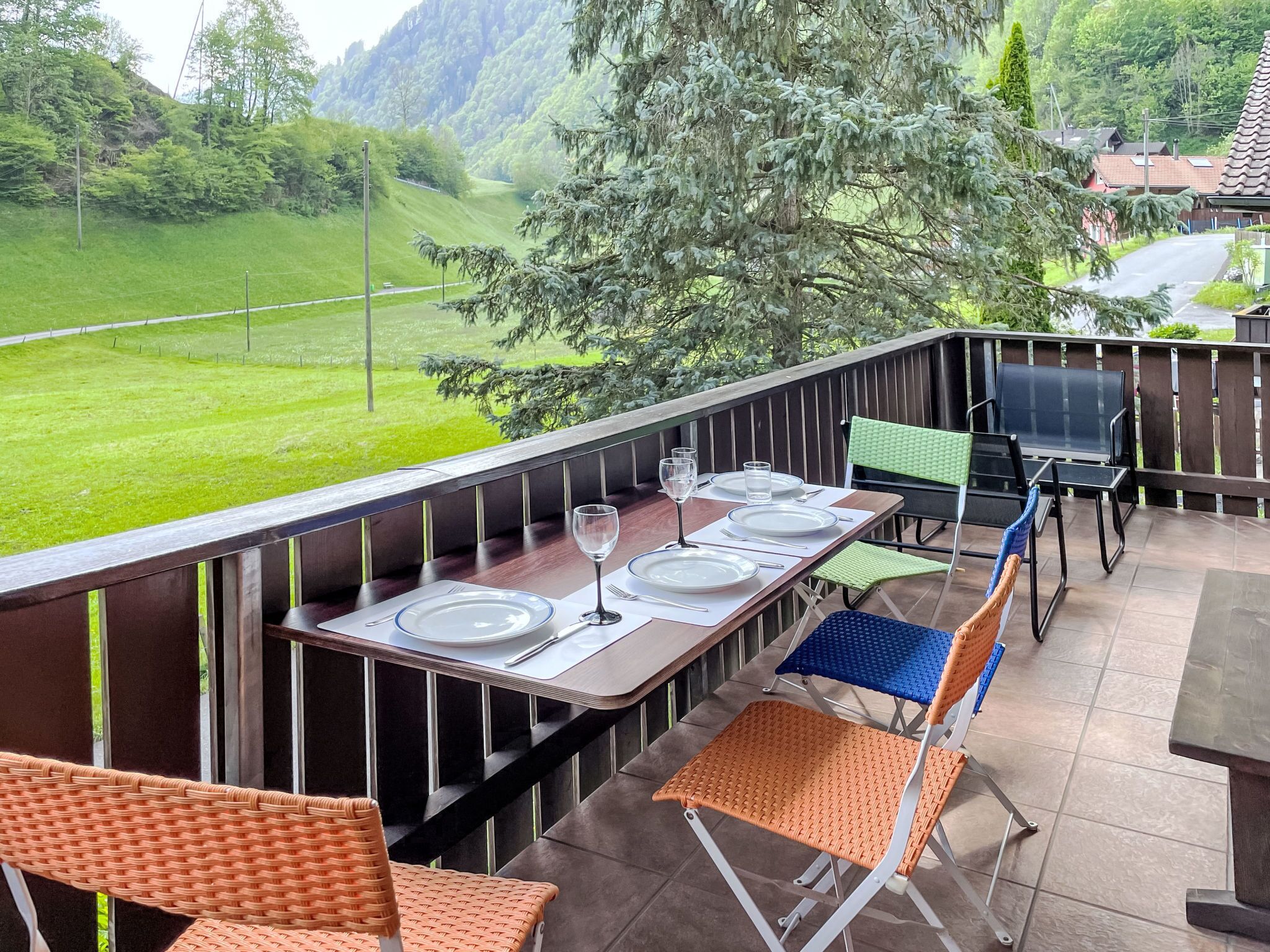 An outdoor dining area with a table set for four, chairs, and a view of a green landscape.
