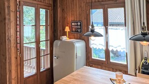 A kitchen with wooden walls, a vintage refrigerator, a wooden table, and a view of a house through the window.