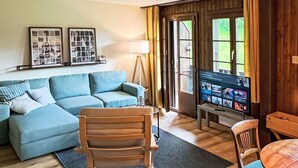A living room with a sofa, a wooden chair, a television, and a door leading outside.