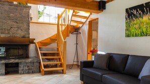 Un salon chaleureux avec une cheminée, un canapé en cuir noir, un escalier en bois et un tableau représentant de l’herbe.