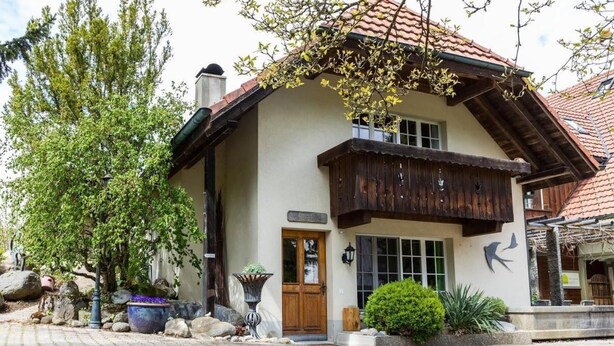 Un bâtiment traditionnel doté d’un balcon en bois, d’un chemin en pierre et d’un jardin bien entretenu agrémenté de rochers et de plantes.