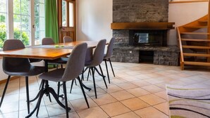 Un espace repas agrémenté d’une cheminée en pierre, de poutres en bois et offrant une vue sur la verdure environnante.