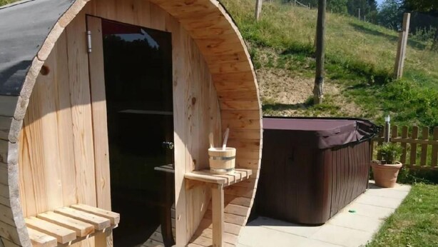 A wooden sauna with a curved exterior, a door, and a small platform with a bucket and brush.