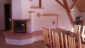 A cozy room with a fireplace, wooden beams, and a dining area with chairs.