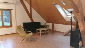 A loft-style room with a sloped ceiling, wooden beams, a sofa, a chair, a small table, and a floor lamp.