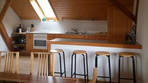 A compact kitchen with wooden cabinets, a central island, and a small dining area with stools.