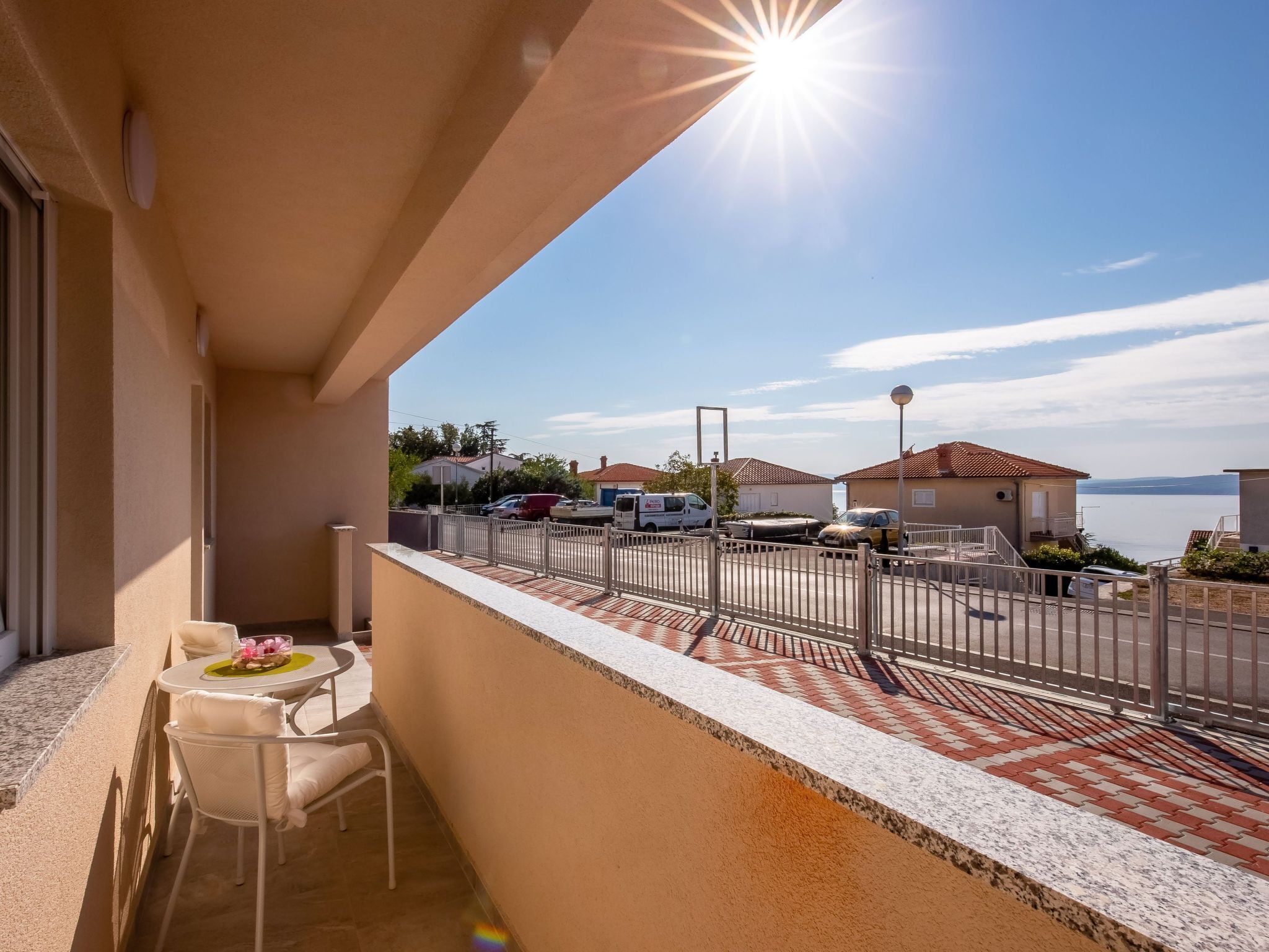 Ein Balkon mit Tisch und Stühlen, Blick auf parkende Autos und Häuser, und ein klarer Himmel.