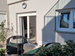 Een terras met een glazen tafel en stoelen, een schuifpui en potplanten.