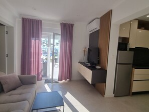 A modern living room with a sofa, a coffee table, and a kitchen area with a refrigerator, microwave, and a flat-screen TV. - Apartment Punta Silo by Interhome (Krk/Šilo)