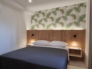 Een moderne slaapkamer met een bed, twee nachtkastjes en een muur met een tropisch bladmotief.