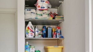 Un lavadero pequeño con una lavadora Bosch, estantes llenos de productos de limpieza y cajas de almacenaje.