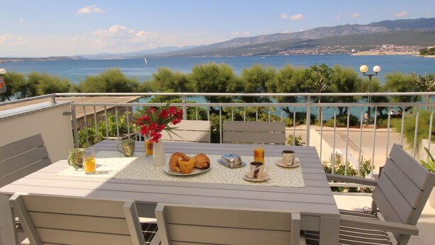 Un balcón con una mesa dispuesta para el desayuno, con vistas a la costa y montañas a lo lejos.