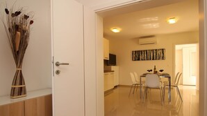 Una cocina moderna con armarios blancos, un comedor con mesa de vidrio y una sala de estar con sofá y televisor.