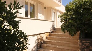 Una escalera conduce a un edificio blanco con persianas, rodeado de follaje.