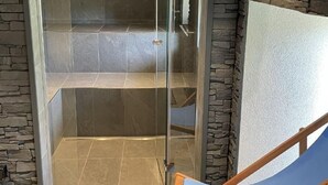 A modern bathroom with a glass shower enclosure, stone wall, and a blue chair. - "Ferme d' Alma" by Interhome (Seleute)