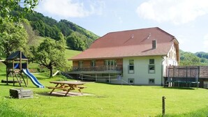 A two-story house with a red-tiled roof, a picnic table, and a playground with a slide. - "Ferme d' Alma" by Interhome (Seleute)
