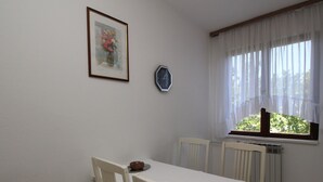 A dining area with a table and chairs, a clock, and a window with curtains. - Apartment Andjela by Interhome (Krk/Šilo)