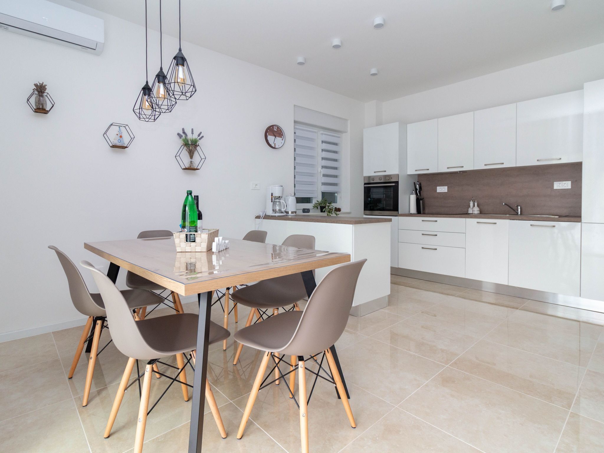 Cozinha moderna com armários brancos, área de refeições com mesa e cadeiras de madeira e luminárias pendentes.