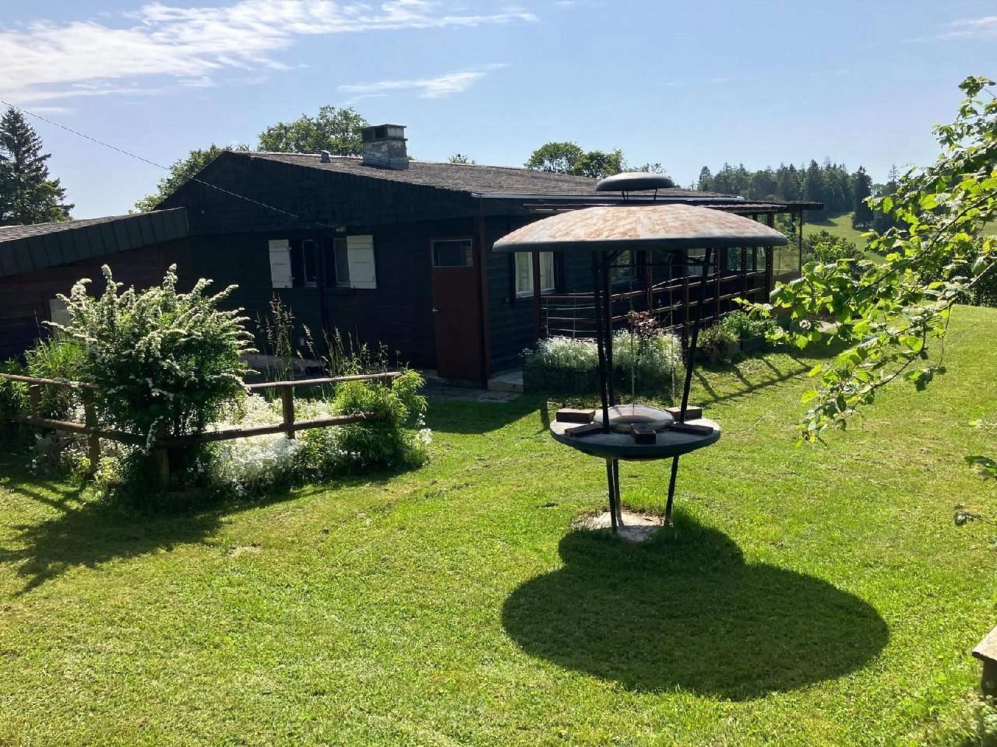 Un jardin avec une table ronde, une clôture en bois et un bâtiment en arrière-plan.