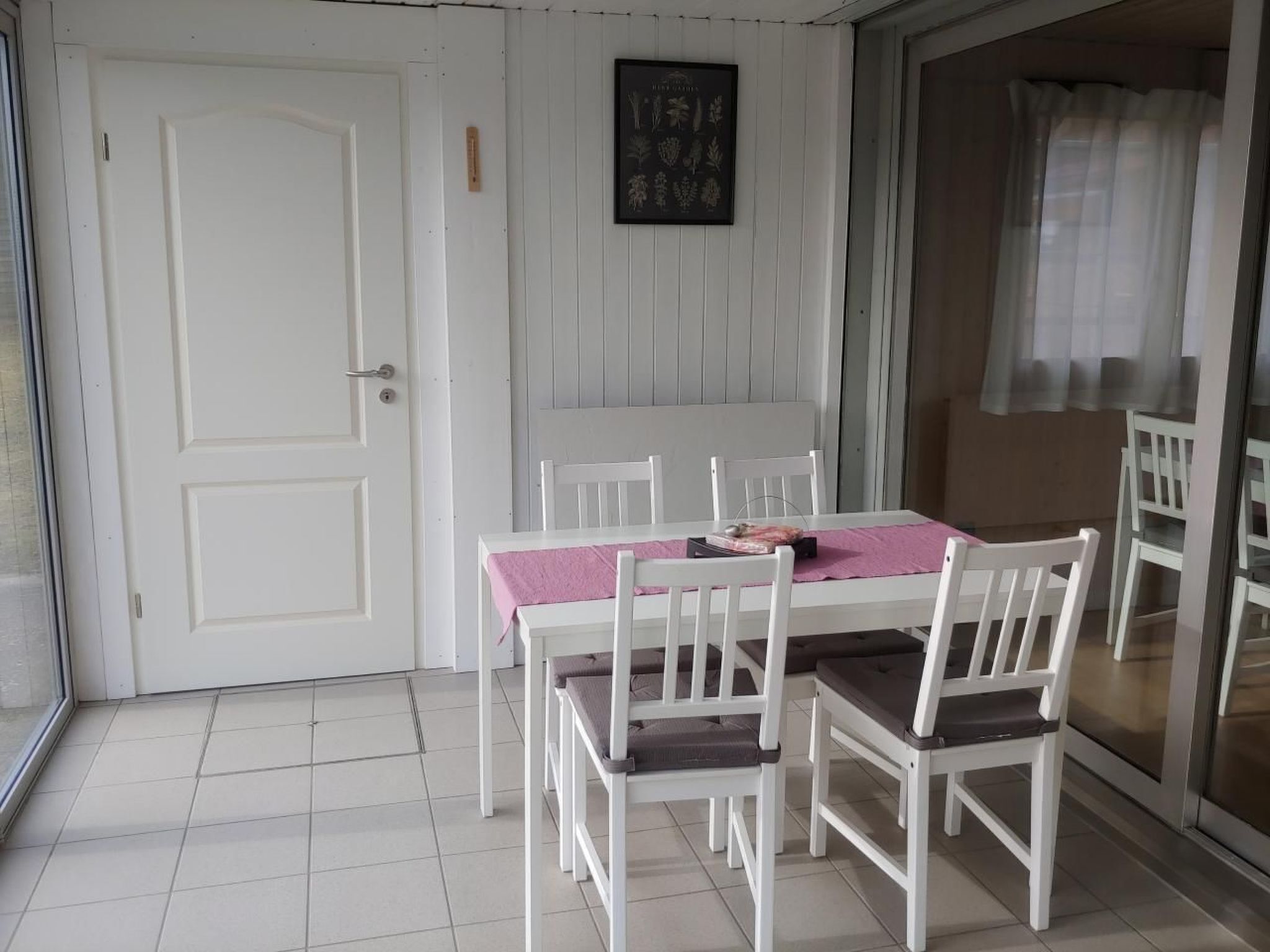 A dining area with a white table and chairs, a pink tablecloth, and a framed botanical print on the wall.