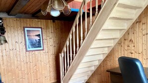 A wooden interior with a staircase, a framed picture on the wall, and a blue chair.