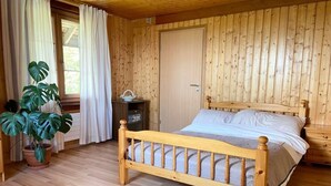 A wooden-paneled room with a bed, a potted plant, and a window with curtains.