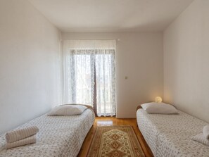 A small, bright room with two single beds, a large window with sheer curtains, and a patterned rug on the wooden floor. - Wohnung Lea in Strandnähe - Agentur TA Leut by Interhome (Privlaka)