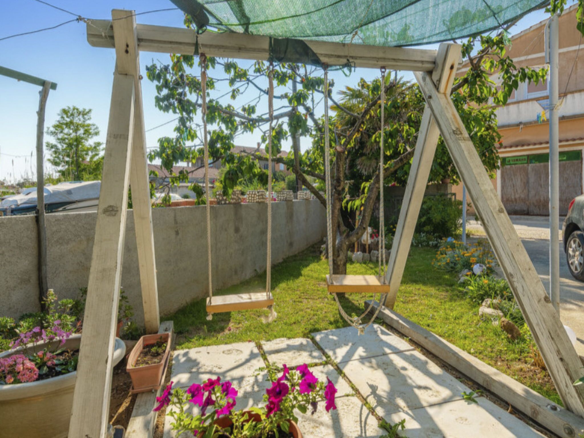 Ein hölzernes Schaukelgerüst in einem Garten mit Blumentöpfen und einer Betonmauer im Hintergrund.