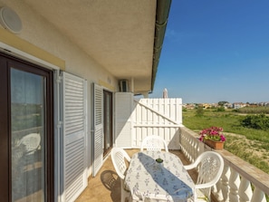 A balcony with a table and chairs, a white fence, and a view of the sea and houses in the distance. - Wohnung Lea in Strandnähe - Agentur TA Leut by Interhome (Privlaka)