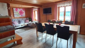 Een gezellig houten blokhutinterieur met een bank, eettafel, stoelen en een televisie.