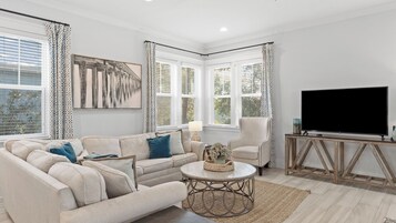A living room with a sofa, armchair, TV, and artwork.