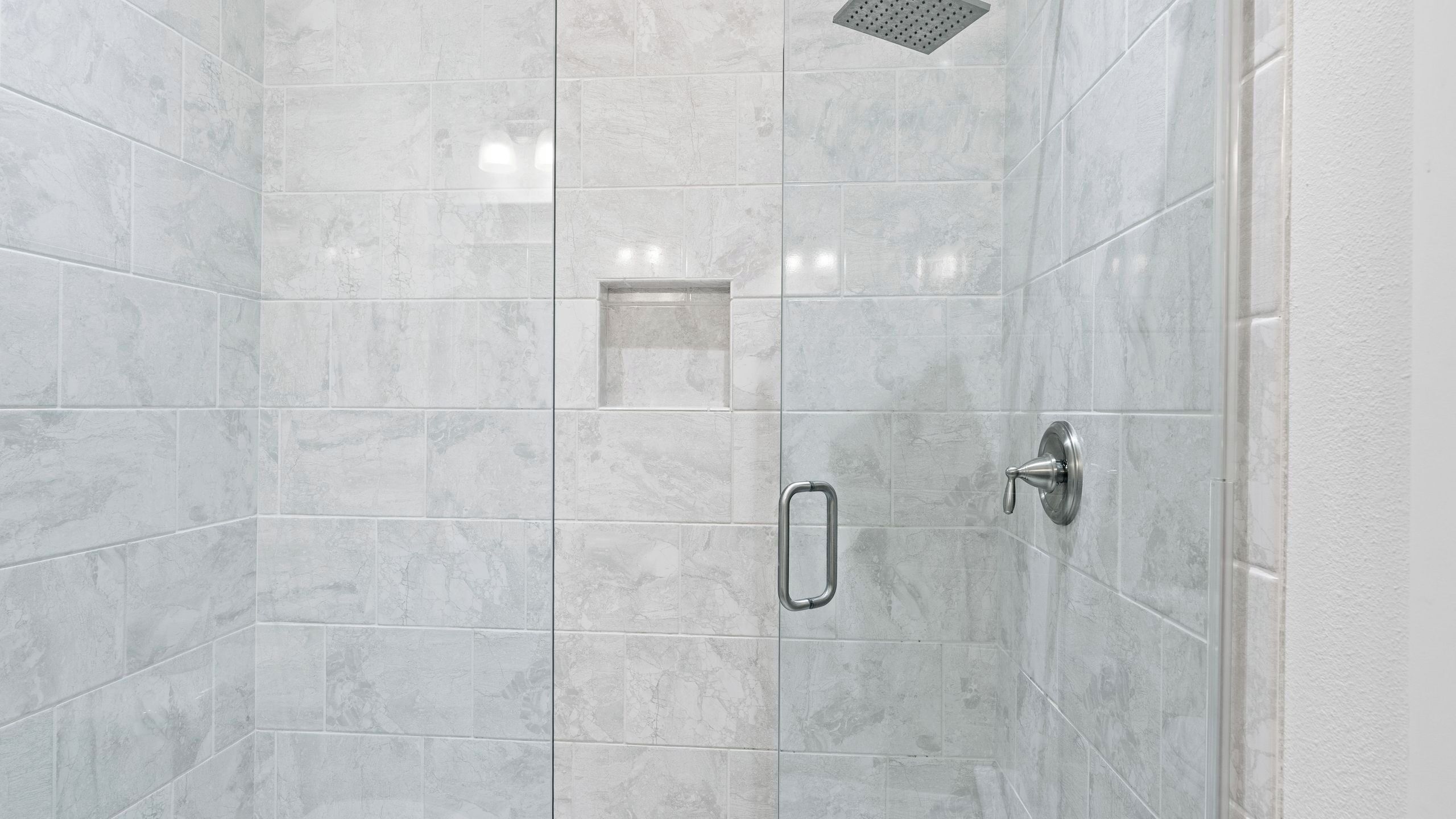 Een douche met een handdouche, een douchekop in een glazen hoek en een metalen handgreep.