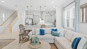 A modern living room with a sofa, coffee table, and a dining area with chairs. - Wind & Sea by Avantstay 30A Retreat Near Gulf Place + Resort-style Communal Pool Access (Santa Rosa Beach)