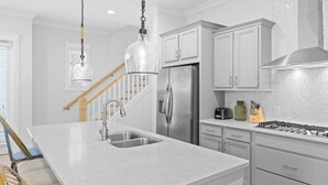 A modern kitchen with a stainless steel refrigerator, a built-in oven, and a large island with a sink. - Wind & Sea by Avantstay 30A Retreat Near Gulf Place + Resort-style Communal Pool Access (Santa Rosa Beach)