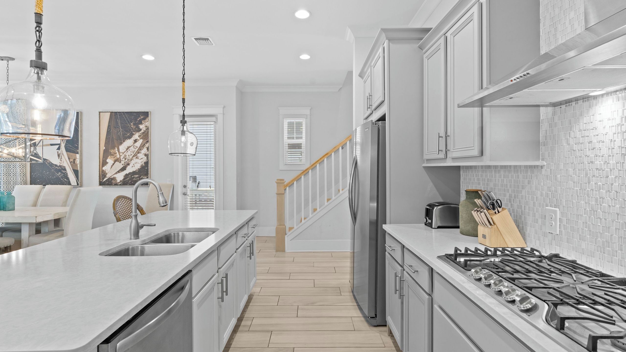 A modern kitchen with a central island, stainless steel appliances, and a wooden staircase leading to a dining area.