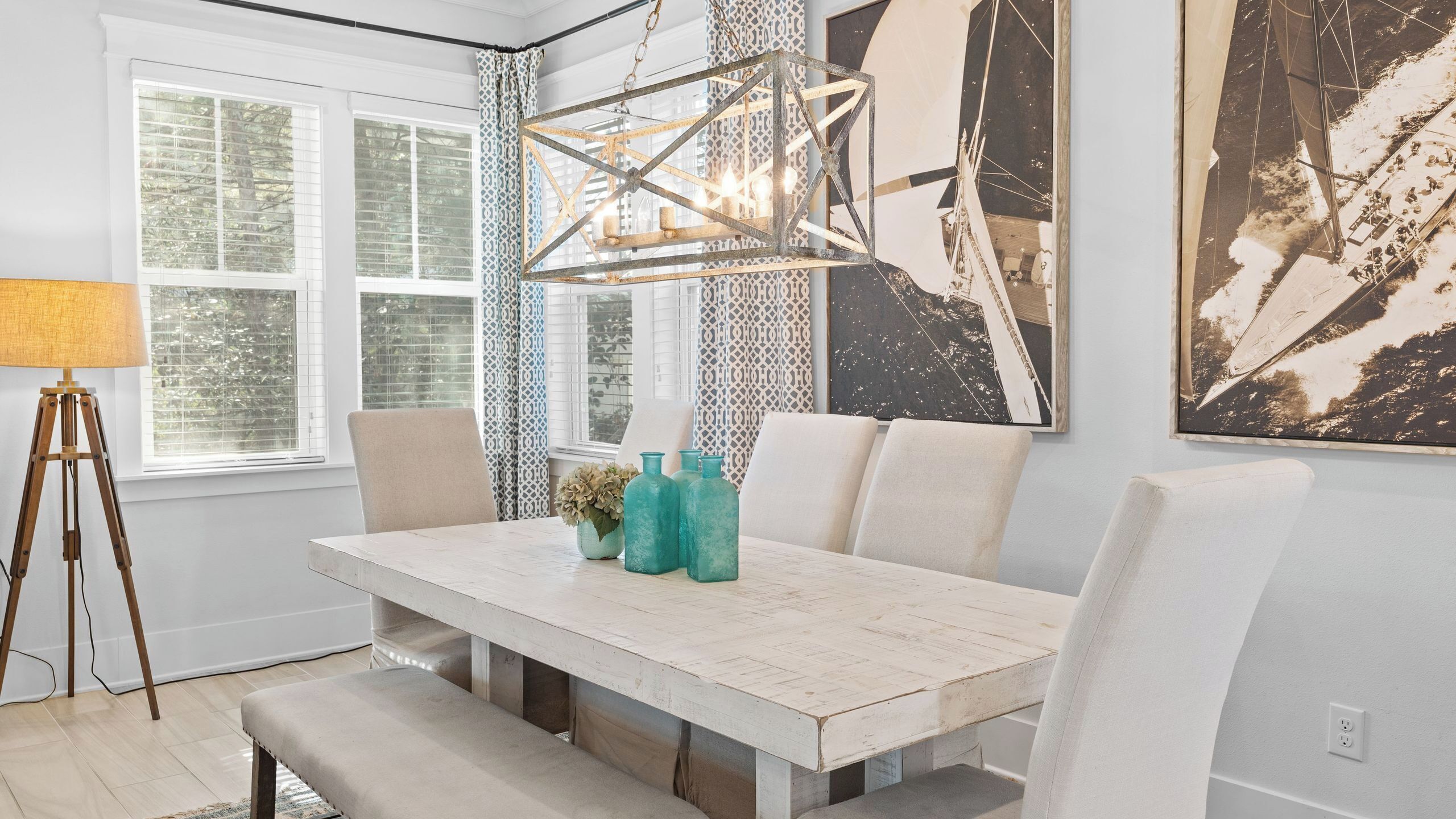 Un espace repas comprenant une table blanche, des chaises, un lampadaire sur trépied et un grand tableau abstrait.