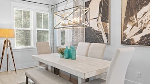 A dining area with a white table, chairs, a tripod floor lamp, and a large abstract painting. - Wind & Sea by Avantstay 30A Retreat Near Gulf Place + Resort-style Communal Pool Access (Santa Rosa Beach)
