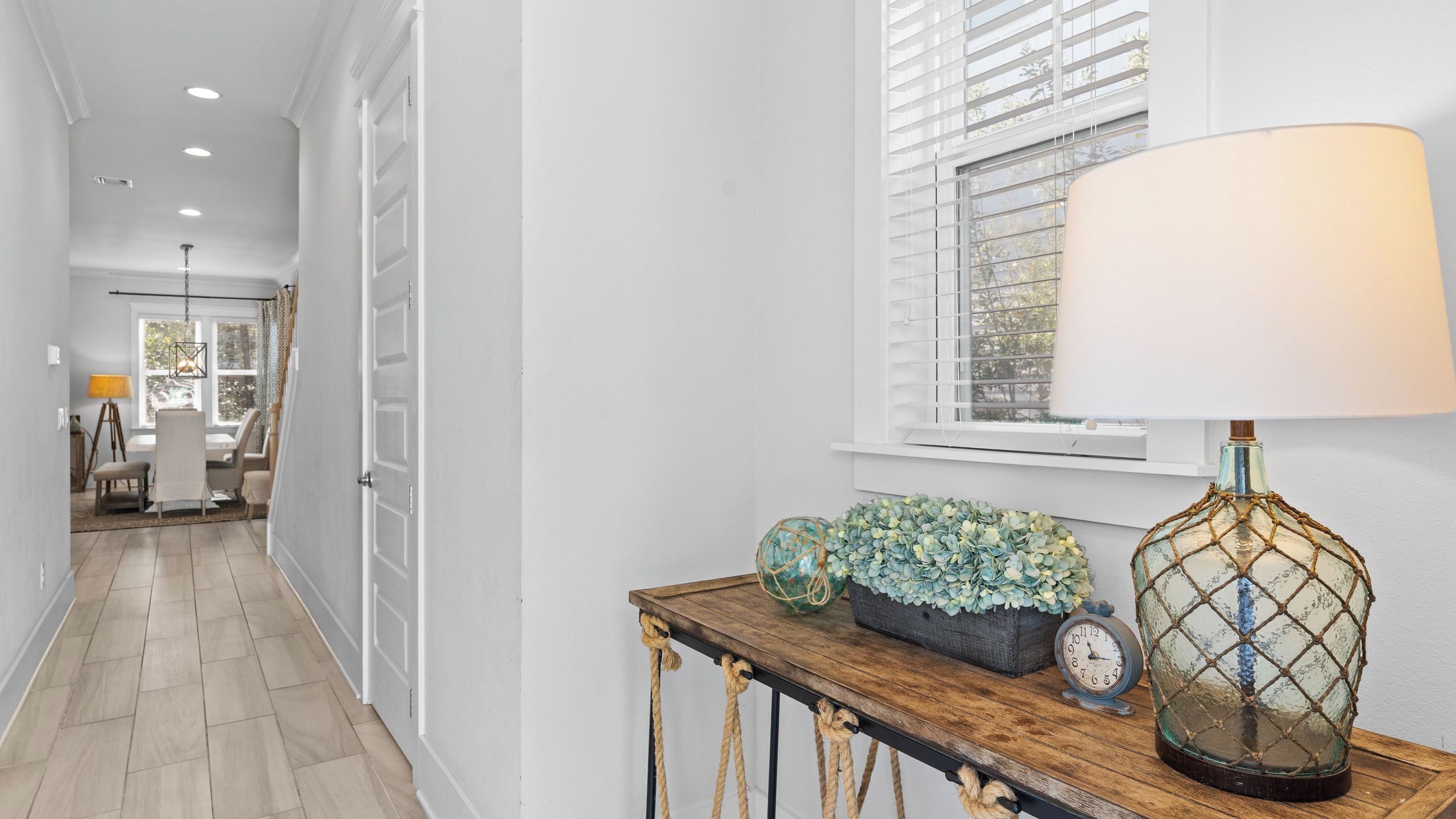 Um corredor com um console de madeira, uma luminária, um relógio e uma planta decorativa.