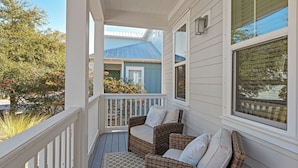 A covered porch with wicker furniture and a view of a blue house. - Wind & Sea by Avantstay 30A Retreat Near Gulf Place + Resort-style Communal Pool Access (Santa Rosa Beach)