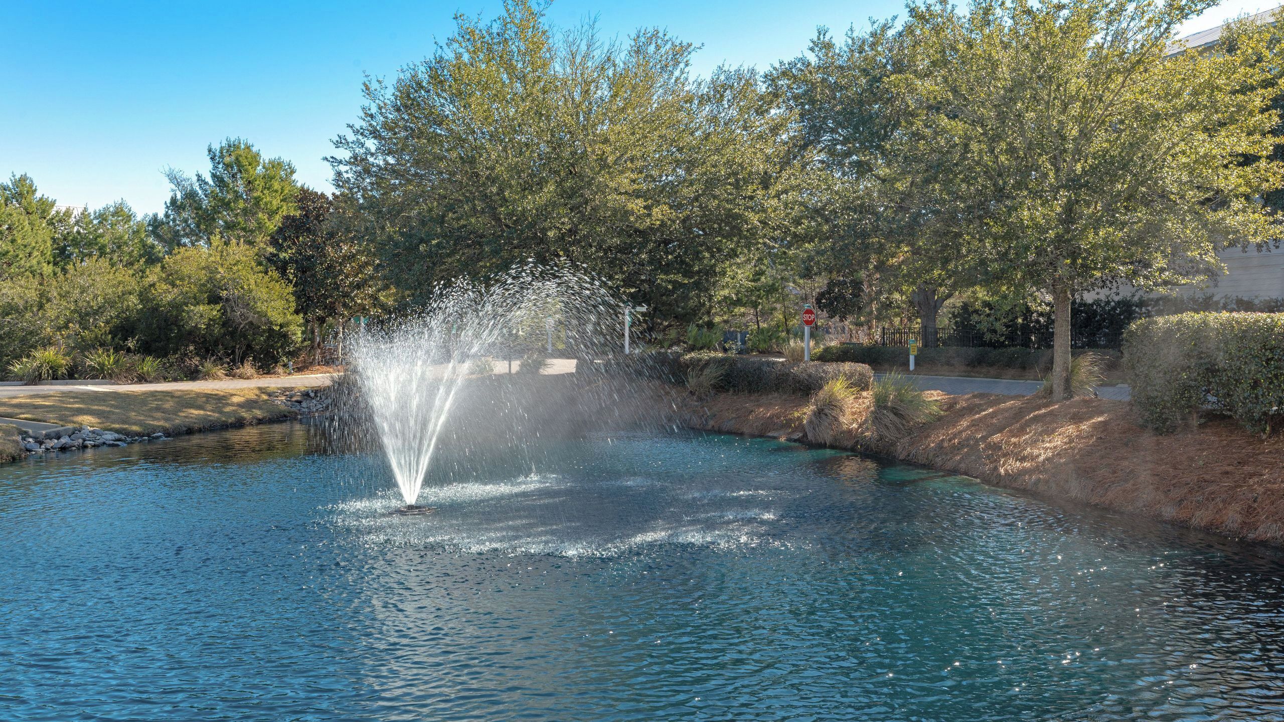 A fountain in a park with a stop sign and trees in the background.