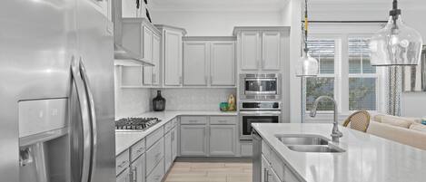 A modern kitchen with stainless steel appliances, white cabinetry, and a large island with a sink.