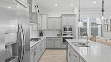 A modern kitchen with stainless steel appliances, white cabinetry, and a large island with a sink.