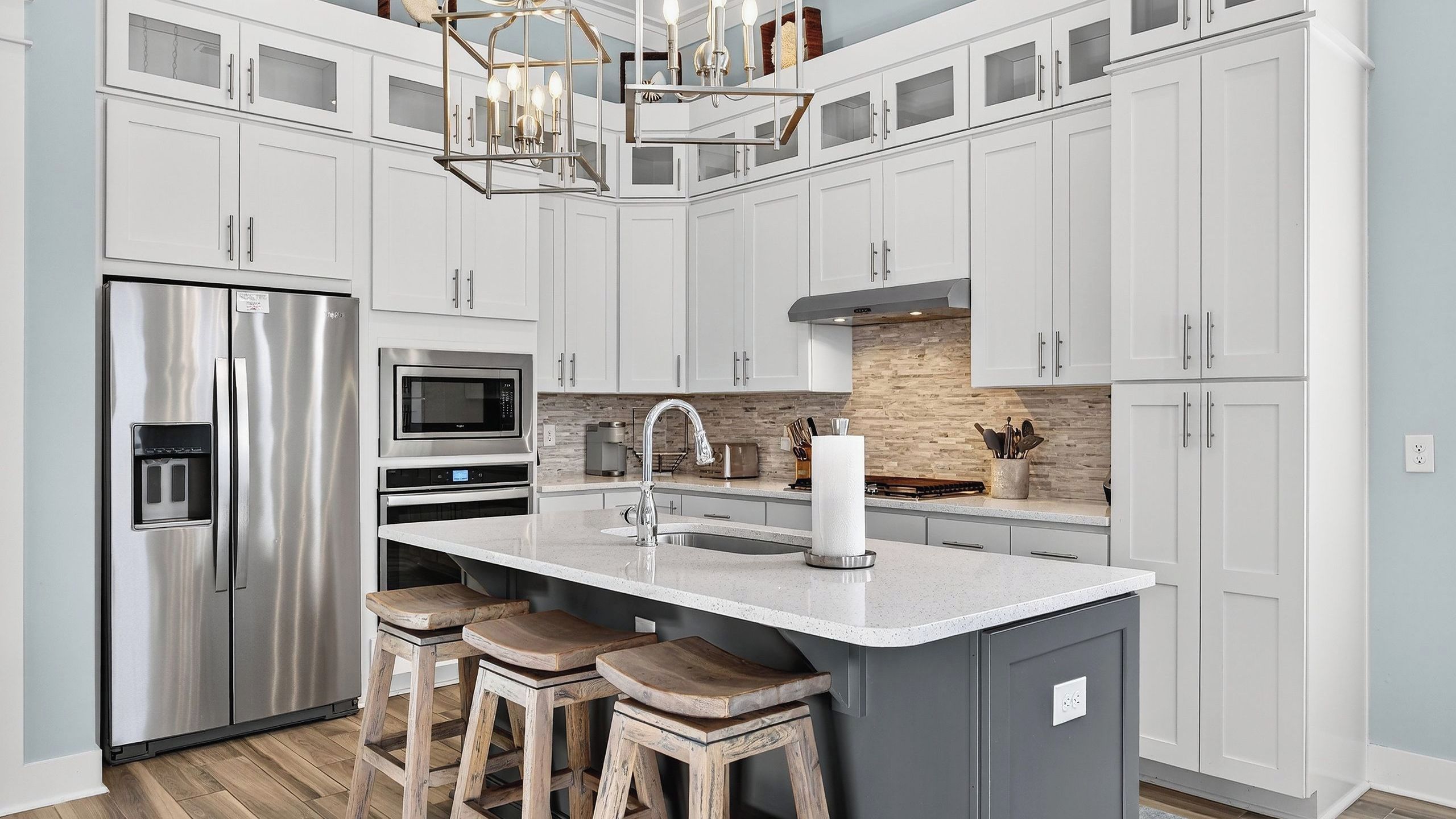 A modern kitchen with stainless steel appliances, a central island with stools, and a stone backsplash.
