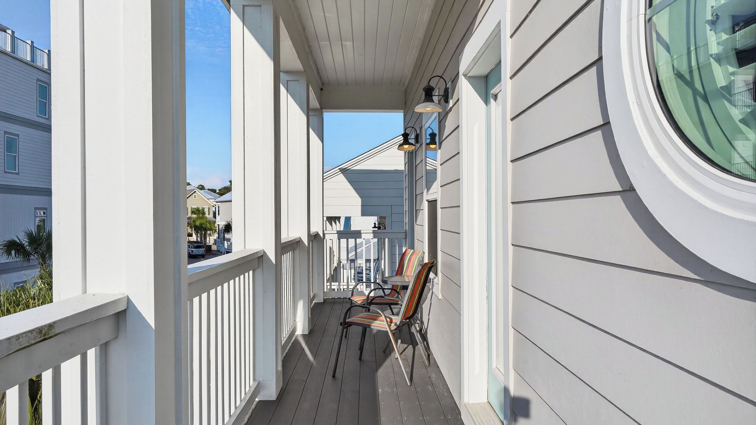 A covered porch with a railing, a chair, and a window with a view of neighboring houses.