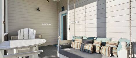 A porch with a swing seat, a table, and chairs.