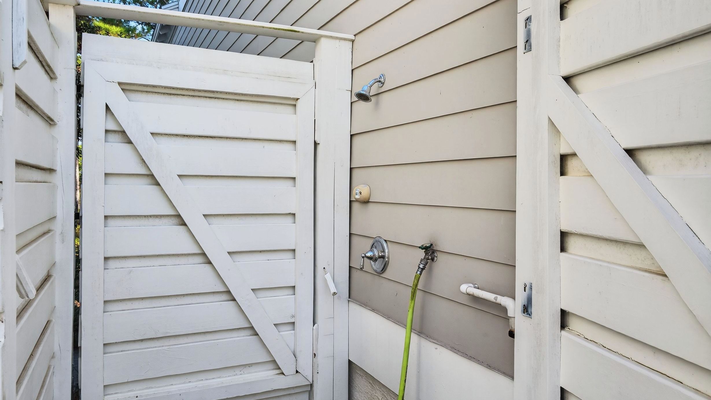 A white exterior wall with a sliding door, a metal faucet, and a hose.