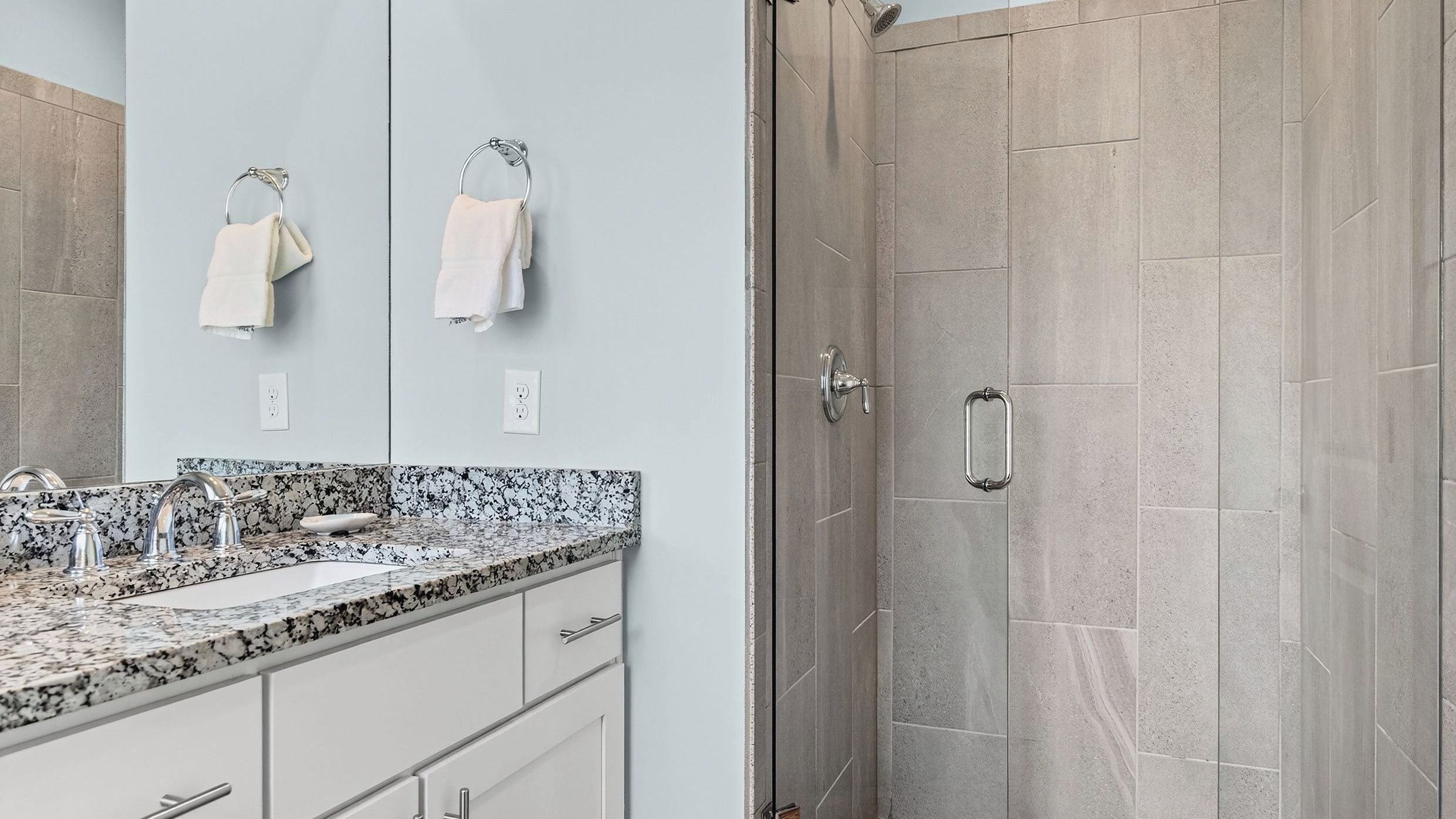 A modern bathroom with a granite countertop, a shower with a glass door, and two towels hanging on a metal rack.