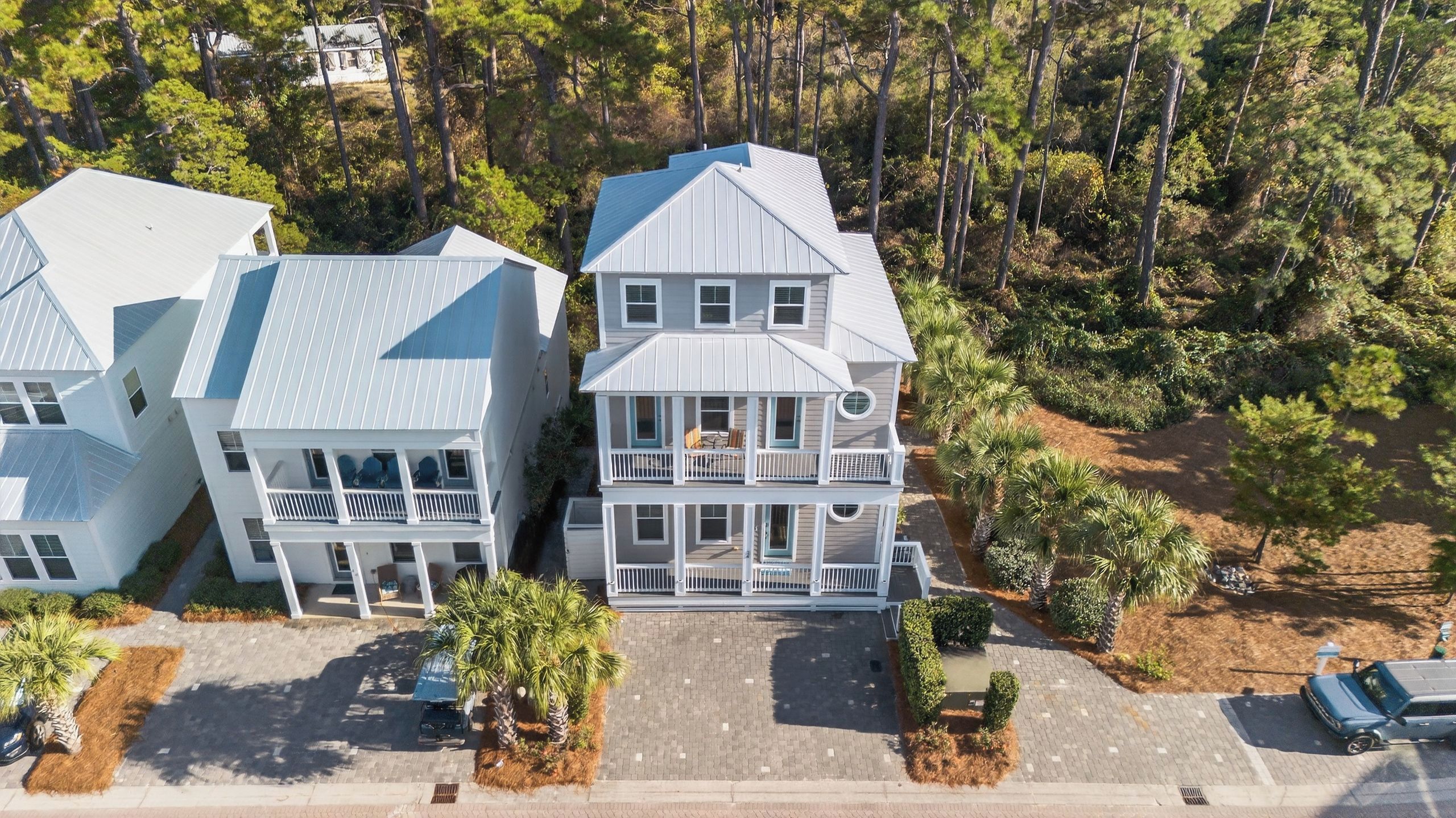 A multi-story residential building with a balcony on the second floor, surrounded by trees and a paved driveway.