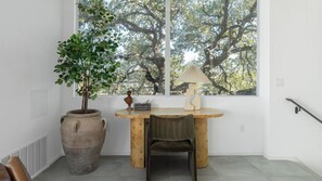 Une piĂšce avec une grande fenĂȘtre, un bureau en bois, une chaise, une plante en pot et une lampe.