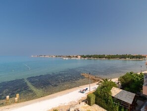 Ein Küstenblick mit einem klaren Strand, einigen Booten und einer entfernten Uferlinie mit Gebäuden.
